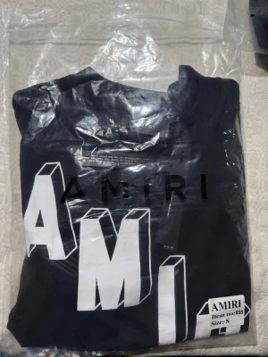 Svart AMIRI t-shirt med stor logga - Säljer en svart t-shirt från AMIRI med stor, vit 3D-logga framtill. T-shirten har rund hals och korta ärmar. Tillverkad i mjuk bomull för en skön känsla och avslappnad passform. Oanvänd bara testat på, allt jag säljer blir väl tagen hand om innan den skickas ut så du får så bra resultat som möjligt.