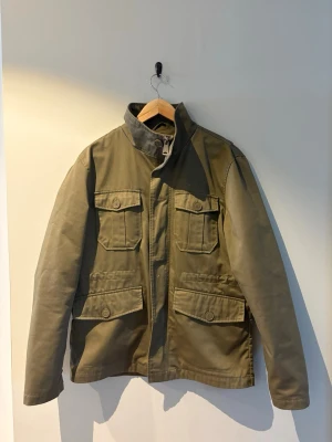 These glory days fieldjacket - Snygg olivgrön fieldjacka från these glory days med fyra stora fickor framtill och hög krage. Jackan har dragkedja och knappar, samt långärmad design. Perfekt för dig som gillar en avslappnad men ändå stilren look. Nypriset ligger på över 2000kr