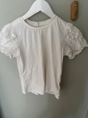 Vit topp med spetsärmar från SHEIN - Söt vit topp från SHEIN med korta puffärmar i spets och rund halsringning. Toppen har en enkel, rak passform och är gjord i mjukt material. Perfekt för dig som gillar romantiska detaljer och vill ha något extra till din outfit.