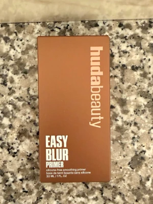 Huda Beauty Easy Blur Primer - helt ny oöppnad - Easy Blur Primer från Huda Beauty är en silikonfri primer som jämnar ut huden och ger en mjuk, slät finish. Förpackningen är brun med vit text och innehåller 30 ml. Perfekt för att skapa en snygg bas innan sminket.