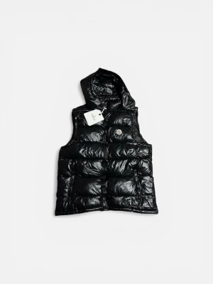 Svart väst från Moncler  - Snygg svart dunväst från Moncler med glansig finish och quiltad design. Västen har en praktisk huva och dragkedja framtill samt Moncler-logga på bröstet. Perfekt för lager-på-lager och streetwear-vibe.