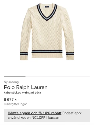 Vit kabelstickad tröja Polo Ralph Lauren - Kabelstickad v-ringad tröja i offwhite från Polo Ralph Lauren. Tröjan har marinblå och svarta ränder vid halsringning, ärmslut och nederkant. Klassisk och sportig look med ribbstickade muddar. Perfekt för dig som gillar preppy stil.