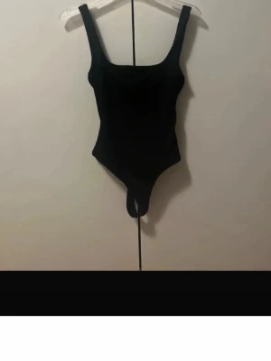 Svart basic body med breda axelband - En enkel och stilren svart body med breda axelband och rundad urringning. Bodyn har klassisk skärning och knäppning i grenen. Perfekt att styla till olika outfits. Materialet ser ut att vara stretchigt och bekvämt.