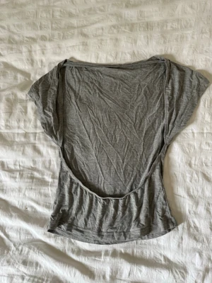 Grå topp med öppen rygg - Säljer en enkel grå topp i mjuk bomull med korta ärmar och en riktigt snygg öppen rygg. Perfekt för dig som gillar minimalistisk stil men ändå vill ha en cool detalj. Passar till både jeans och kjol.