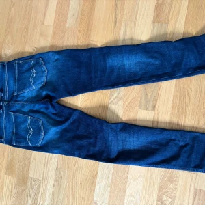 Replay Anbass jeans i mörkblå denim - Säljer ett par Replay Anbass jeans i mörkblå tvätt med snygga slitningar. Klassisk femficksmodell med dragkedja och smal passform. Perfekta för dig som gillar stilrena jeans med lite edge.för fler bilder kontakta mig.nypris 1200kr.