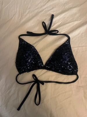 Svart bikini med paljetter och knyt - Snygg svart bikini från calzedonia med paljetter på både överdel och underdel. Triangelformad topp med knyt i nacken och ryggen samt matchande trosa med knyt i sidorna. Perfekt för dig som vill sticka ut på stranden!