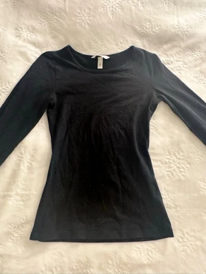 Svart långärmad topp H&M - En enkel svart långärmad topp från H&M med rund halsringning. Modellen är figurnära och passar perfekt till jeans eller kjol. Tillverkad i mjuk bomull som känns skön mot huden.
