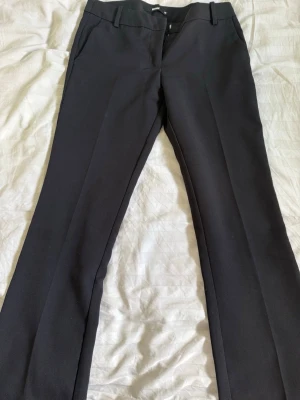 Svarta kostymbyxor från Bik Bok - Snygga svarta kostymbyxor från Bik Bok Vera. De är uppsydda då jag är 167 cm men går att sprätta upp utan problem. Lågmidjade. Byxorna har diskreta sidofickor och stängs med hake och dragkedja. Perfekta för en clean och stilren look.