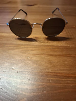 Runda solglasögon med guldfärgade bågar - Snygga solglasögon från H&M med rund form och tunna guldfärgade metallbågar. Glasen är mörka och ger en retroinspirerad look. Perfekta för dig som vill sticka ut med en klassisk och tidlös stil.