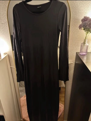 Svart långärmad långklänning - En enkel och stilren svart långklänning från Monki med rund halsringning och långa ärmar. Klänningen har en rak passform och är tillverkad i mjuk bomull, perfekt för en clean och avslappnad look.