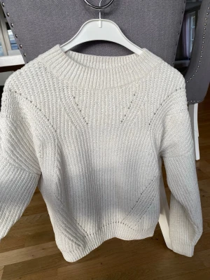 Vit stickad tröja från H&M - Säljer en vit stickad tröja från H&M med ribbad struktur och diskreta mönsterstickningar. Tröjan har rund halsringning och långa ärmar, perfekt för kyliga dagar. Materialet är mjukt och bekvämt. Har ett litet slitage bak men annars fint i skick. Köparen står för frakt.
