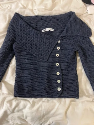 Mörkblå stickad tröja från Zara - Trendig mörkblå stickad tröja från Zara med bred krage och dekorativa vita knappar längs sidan. Tröjan har lång ärm och är gjord i ett grovt stickat material som ger en cool och avslappnad look.