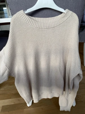 Beige stickad tröja från Kappahl - Snygg beige stickad tröja från Kappahl med bred ribbad rundhals och ribbade muddar. Tröjan har en avslappnad passform och är perfekt för lager på lager. Köparen står för frakt.