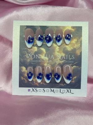 Sthlm (XS);Medium Almond - Snygga handgjorda press-on naglar i en medium lång mandelform. Naglarna har en nude bas med handmålad vit french-tip och dekoreras med små blå blommor och silverdetaljer. Perfekt för dig som vill ha en unik och trendig look. XS: 14 mm, 11 mm, 11,5 mm, 10 mm, 8 mm 