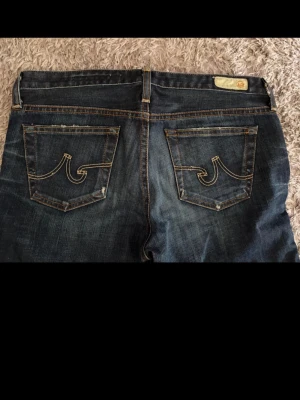 Mörkblå jeans från True Religion - Säljer ett par mörkblå jeans från adriano jeans med ikoniska kontrastsömmar och broderade bakfickor. Jeansen har slitna detaljer och skinny passform. Perfekta för dig som gillar en avslappnad men ändå trendig look. Midja: 80 cm benlängd:78 cm 