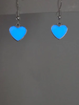 Blå lysande hjärtformade örhängen - Säljer ett par unika örhängen i rostfritt stål med hjärtformade hängen som lyser i blått i mörker efter att de har varit en kort stund i vanligt dagsljus eller solljus. Efter normal användning kan de lysa upp till 12 timmar. Örhängena har silverfärgade detaljer och en modern, ungdomlig design. Perfekta för dig som vill sticka ut och addera lite glow till din stil. Örhängena tål vatten & har en mycket lång livslängd. Handgjorda. 
