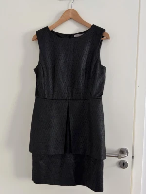 Tiger Of Sweden klänning - Storlek 38 - Snygg svart ärmlös kortklänning från Tiger of Sweden med diskret mönster och rund halsringning. Klänningen har en stilren, figurnära passform och ett lager-på-lager-utseende framtill. Perfekt för dig som gillar enkel men elegant stil.