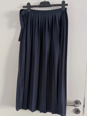 ARKET marinblå klänning/kjol - Storlek XS  - Snygg mörkblå plisserad klänning (går även användas som kjol) med knyt och dragkedja på sidan. Den har ett elegant fall och passar perfekt till både sneakers och boots. Tillverkad i ett mjukt och följsamt material som ger en skön känsla hela dagen.