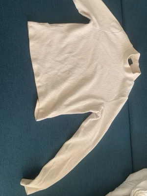 Vit ribbad polotröja - Säljer en vit långärmad polotröja med ribbad struktur. Tröjan har en hög krage och är gjord i ett mjukt, stretchigt material som sitter skönt på kroppen. Perfekt att styla lager på lager eller bära som den är. Det är storlek XL men passar även L/M 