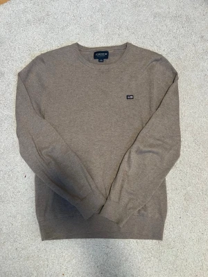 Beige stickad tröja Lexington - Klassisk beige stickad tröja från Lexington med rund halsringning och diskret logga på bröstet. Tröjan har ribbade muddar vid ärmslut och nederkant. Är i storlek 170, nästan aldrig använt så är i väldigt fina skick!