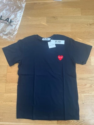 Svart Comme des Garçons PLAY t-shirt - Svart t-shirt från Comme des Garçons PLAY med det ikoniska röda hjärtat broderat på bröstet. Klassisk passform och rund halsringning. Tillverkad i mjuk bomull, perfekt för en clean och stilren look.