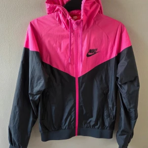 Nike Vindjacka  - En vindjacka med luva i neonrosa/svart från Nike. Storlek M men liten i storleken, sitter som S. Toppenfint skick! Har fickor framtill.