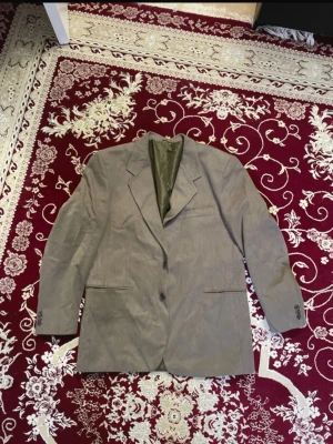 Khaki Kavaj med grön insida - Stilren khaki kavaj med klassisk passform och grön insida. Kavajen har två knappar framtill, tre knappar vid ärmslut och två fickor med lock. Det står tyvärr inte viken storlek det är, men jag gissar på att den skulle passa en strl L-XL.