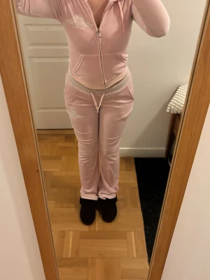 Ljusrosa  mjukisset Vintage Juicy Couture - Säljer ett ljusrosa  mjukisset från Juicy Couture vintage modell. Setet består av en ziphoodie med fickor och matchande byxor med dragsko i midjan. Båda delarna har vita detaljer och broderad logga. Jag är 166 och midelllen på byxorna är långa på mig. Storlek Xxs i båda men passar även en som brukar ha storlek S