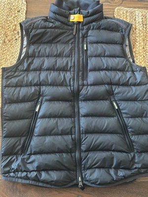 Svart dunväst från Parajumpers - Snygg svart dunväst från Parajumpers i superlätt material. Västen har hög krage med gul detalj, tre dragkedjeförsedda fickor och quiltad design. Perfekt för lager-på-lager och streetwear-vibe. Märkt med Super Lightweight på insidan.