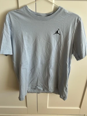 Ljusblå Jordan t-shirt - Snygg ljusblå t-shirt från Jordan med klassisk Jumpman-logga broderad på bröstet. T-shirten har rund halsringning och korta ärmar. Perfekt för en sportig och avslappnad stil.