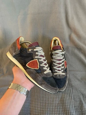 Philippe Model  - Snygga sneakers från Philippe Model i en mix av grå mocka och mörkblå nylon. Skorna har vinröda detaljer på plös och häl, samt beigea skosnören och sula. Klassisk låg modell med logga på sidan och retrovibbar.