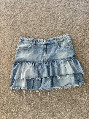 Blå jeanskjol med volanger - Säljer en kort jeanskjol i blå denim med två lager volanger och råa kanter. Kjolen har fickor fram och bak samt bälteshällor i midjan. Perfekt för dig som gillar en avslappnad och trendig stil. Aldrig använd💞