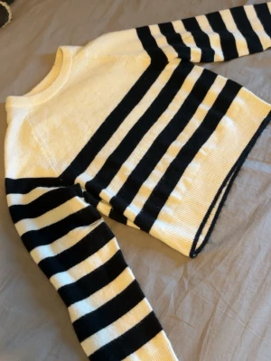 Randig stickad tröja i svart och vitt - Säljer en snygg stickad tröja med breda svarta och vita ränder. Tröjan har rund halsringning, långa ärmar och ribbade muddar. Perfekt för dig som gillar klassisk men trendig stil. Materialet känns mjukt och bekvämt.