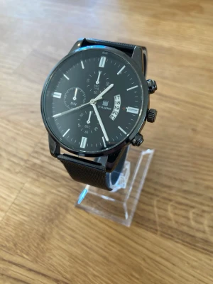 Shaarms Chrono Mesh 42mm Herrklocka - Svart SHAARMS armbandsur med en svart urtavla och silver-vita markeringar. Klockan har tre sub-urtavlor och en datumvisning. Boetten är svart och matchas med ett svart meshband. Klockan drivs av ett kvartsurverk. Kronografen är estetisk. Fint använt skick enligt bilder. Har helt nytt batteri och fungerar utmärkt.  Nypris: 400 SEK Mitt pris: 289 SEK  Skickas alltid snabbt och spårbart. Skriv vid frågor och se gärna mina andra annonser!   GRATIS: För betalande kunder erbjuder jag personlig experth