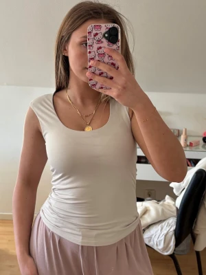 KrämVit ärmlös linnetopp i mikrofiber - Säljer en enkel och stilren vit linnetopp med rundad urringning och tight passform. Toppen är ärmlös och gjord i ett mjukt, stretchigt material som sitter snyggt på kroppen. Perfekt att matcha med jeans eller kjol för en clean look.