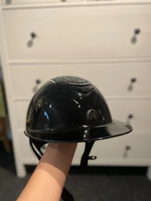 Svart ridhjälm med glitter och stenar - Onek Avance Glossy Swarovski-hjälm - svart, skal 2 Sparsamt använd, nypris 5599kr Slutade ridning och därför hann den inte användas så mycket. Alla stenar sitter, inga repor. Originalpåse & kartong! Linern ingår. Säljes för 3200kr