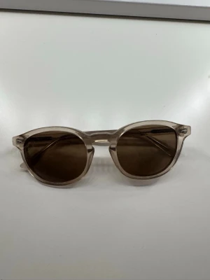 Beige runda solglasögon - Snygga solglasögon med rundad form och transparent beige båge. Glasen är mörka och ger en cool kontrast till den ljusa ramen. Perfekta för soliga dagar och en stilren look.