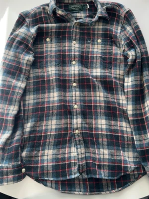 Rutig skjorta från Ralph Lauren - Säljer en klassisk rutig skjorta från Ralph Lauren Polo Country i blått, vitt och rött. Skjortan har lång ärm, knappar framtill och två bröstfickor. Tillverkad i mjuk bomull och har en custom fit-passform.