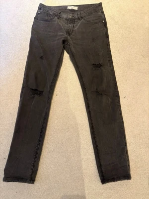 Gråa jeans Celio 31/30 - Säljer ett par gråa skinny jeans med slitningar på båda benen. Jeansen har klassisk femficksmodell och dragkedjegylf. Snyggt slitna detaljer för en trendig look. Perfekta för dig som gillar en avslappnad och edgy stil. Celio från Colombia storlek 31. Står 32 men sitter perfekt lite mina övriga 48 / 31. 