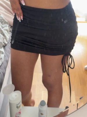 Svart miniskirt - Säljer en svart kortkjol med snörningsdetalj på sidan. Kjolen har en tight passform och är gjord i ett mjukt, stretchigt material som sitter snyggt på kroppen. Perfekt för dig som vill ha en enkel men trendig kjol till garderoben🥰