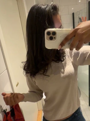 Beige ribbad långärmad topp - Snygg beige ribbad långärmad topp med rund halsringning. Materialet är mjukt och stretchigt, vilket gör den bekväm att bära. Passar perfekt till jeans eller kjol för en enkel och stilren look. Finns en liten svart fläck på ena ärmen