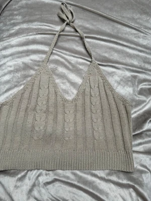 Beige stickad halterneck linnetopp - Snygg beige stickad linnetopp med halterneck och knyt i nacken. Toppen har ribbade detaljer och kabelstickat mönster framtill. Perfekt för dig som gillar en croppad och trendig look.Rök och djurfritt hem. Pruta gärna !🌸