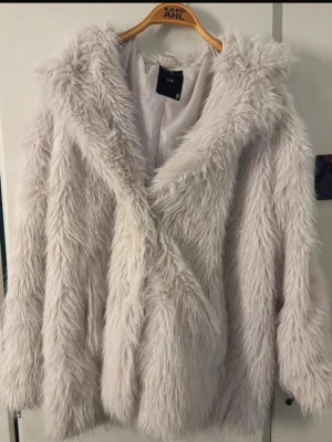Vit fluffig pälsjacka  - Supersnygg vit pälsjacka från lager med fluffig look och stora slag. Jackan har långa ärmar, knappar framtill och är fodrad på insidan. Perfekt för dig som vill sticka ut med en trendig och mysig vinterstil.