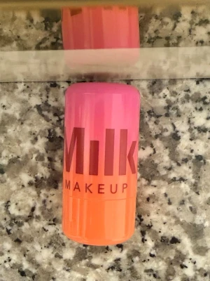 Milk Makeup – Cooling Water Jelly Tint (lip & cheek stain) - Säljer ett rouge i stickform från Milk Makeup. Förpackningen är i en snygg gradient av rosa och orange plast, och själva rouget har en intensiv orange ton. Perfekt för att ge kinderna en fräsch och färgstark look.