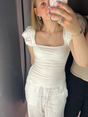 Vit ribbad topp med volangärm H&M - Supersöt vit topp från H&M med ribbad struktur och volang ärmar. Fyrkantig ringning och tight passform som framhäver figuren. Perfekt till både jeans och kjol för en trendig look.