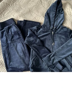 Mörkblå velourset från Juicy Couture - Mysigt loungewear-set i mörkblå velour från Juicy Couture. Setet består av en ziphoodie med dragsko och fickor samt matchande byxor med resårmidja och fickor. Perfekt för chill dagar hemma eller när du vill vara extra bekväm. Överdel s underdel xs!