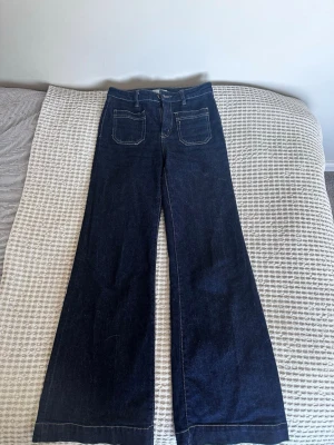 Trendiga jeans från Gina - Snygga mörkblå jeans med vida ben och två stora fickor framtill och markerade sömmar. Perfekta för dig som gillar retrostil och vill sticka ut lite extra. Materialet är klassisk denim.