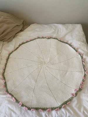 Virkad rund filt med blommor - Handgjord virkad rund filt i vit bomull med gröna blad och rosa blommor. Från mitten till kant är det 40 cm 