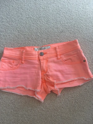 coral rosa shorts från Abercrombie & Fitch - Säljer ett par coral rosa shorts från Abercrombie & Fitch med råa kanter och klassisk femficksdesign. Shortsen har knappgylf och bälteshällor, samt snygga bakfickor med dekorativ söm. Perfekta för sommardagar!