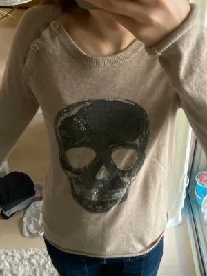 Beige stickad tröja med döskalle -  Superfin ljusbrun Cachemire tröja från Zadig Voltaire med dödskalle på framsidan och knappar vid ena ärmen. Köpt på arkivet men är knappt använd.